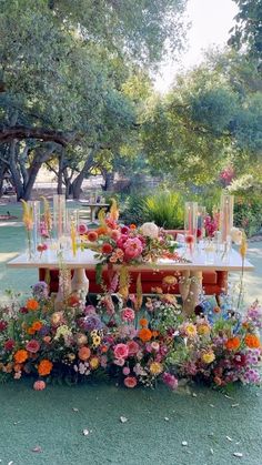 a table with flowers and candles on it in the middle of a park surrounded by trees