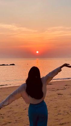 a woman standing on top of a sandy beach next to the ocean with her arms outstretched