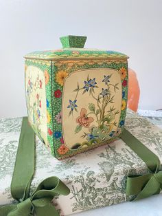 a decorative box sitting on top of a pile of books next to a green ribbon