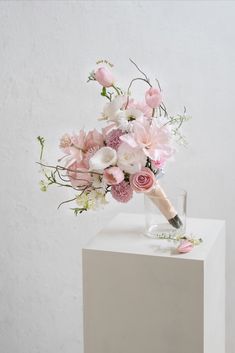 a bouquet of pink and white flowers in a vase on top of a block of concrete