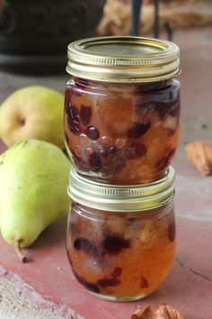 two jars filled with fruit sitting on top of a table next to pears and walnuts