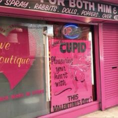 a pink store front with signs on the windows and doors that say cupid, valentine's day or both him and her