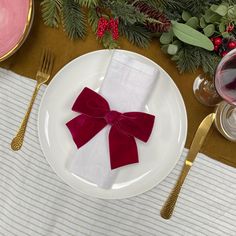 a white plate topped with a red bow on top of a table next to silverware