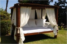 a bed with white pillows and curtains on top of it in the middle of some grass