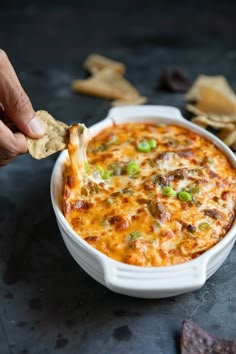 a hand dipping a cracker into a casserole dish