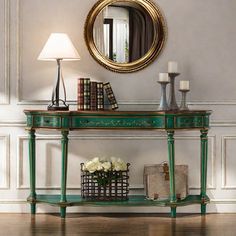 a green console table with flowers and books on it in front of a round mirror