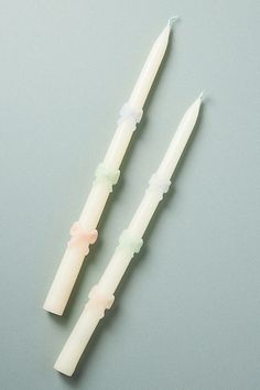 two white candles sitting next to each other on a gray surface with one candle lit