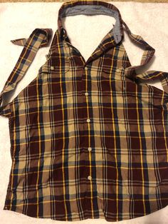 a brown and yellow plaid shirt laying on top of a white sheeted floor next to a pair of scissors