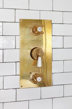 a gold faucet on a white brick wall next to a toilet paper dispenser