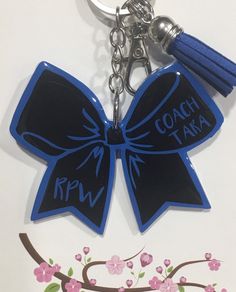 "This personalized tag will make a great gift for your cheerleader, coach, or even for the entire team! It's perfect for their cheer bag, backpack, gym bag, team bag and much more. When checking out, please include the following in \"Notes to Seller\" section: 1. Primary Color (color of ribbon) 2. Secondary Color (color of trim and lettering) 3. Name, Monogram or Initial ** DETAILS ** - 1 acrylic tag / key chain - Approx 2\" tall & 3\" in wide - Premium adhesive vinyl - Keychain hardware." Customized Black Keychains For Personal Use, Customizable Black Keychains For Personalized Gifts, Customizable Black Keychain For Personalized Gift, Cheer Keychain, Sports Bag Tags, Cheer Bag, Custom Backpack, Team Bags, Backpack Tags