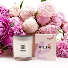 a candle and some pink flowers on a white surface with a box in the foreground