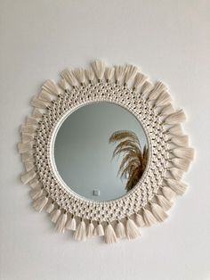 a round mirror with tassels hanging on the wall next to a white wall