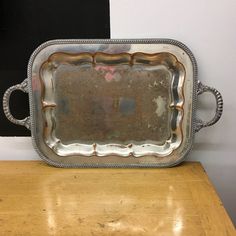 an antique silver tray with handles on a wooden table