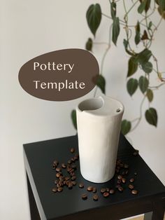 a white vase sitting on top of a black table next to coffee beans and a potted plant