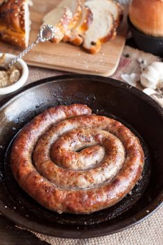 two sausages in a frying pan on a table with bread and other foods