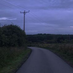 an empty road with power lines in the distance and trees on both sides at dusk