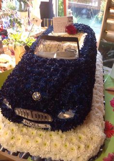 a blue car cake sitting on top of a table next to other cakes and flowers