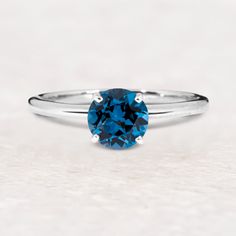 a blue diamond ring sitting on top of a white surface with the center stone in the middle