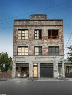 an old brick building with two garages on the side and one car parked in front