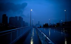 an empty walkway in the middle of a city at night with street lights and dark clouds