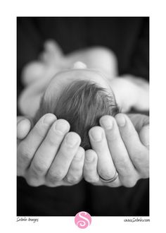 a black and white photo of two hands holding a baby's head in the middle