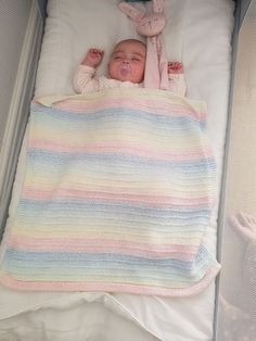 a baby laying in a crib next to a stuffed animal and some blankets on top of it