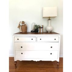 a white dresser sitting on top of a wooden floor next to a lamp and vase