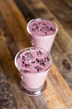 two glasses filled with pink smoothie on top of a wooden table next to each other