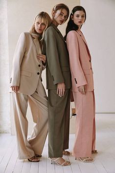 three women standing next to each other in front of a white wall wearing different colored suits