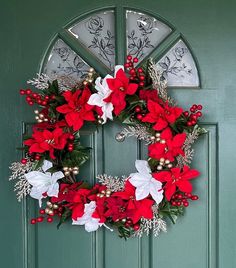 a wreath with poinsettis and greenery hangs on a green door