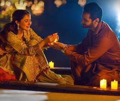 a man and woman sitting next to each other with candles on the ground in front of them