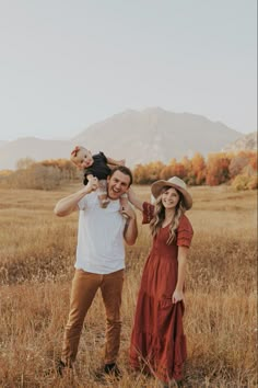 a man holding a baby in his arms while standing next to a woman wearing a hat