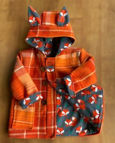 an orange jacket with foxes on it is sitting on a wooden floor and has its hood up