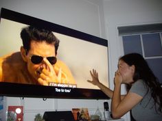 a woman standing in front of a large television screen with the image of a man on it