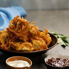 a bowl filled with fried food next to two small bowls full of dipping sauces