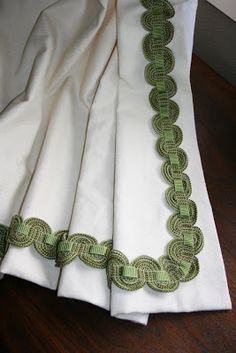 four white and green napkins with decorative trim on them sitting on a wooden table