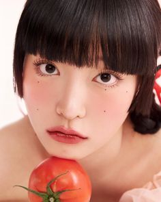 a woman holding a tomato in her right hand and looking at the camera with an evil look on her face