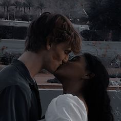 a man and woman kissing each other in front of trees