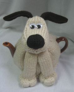 a knitted dog sitting on top of a white sheet with a tea pot in it's mouth