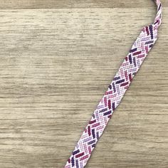 the pink and white braided bracelet is laying on a wooden surface