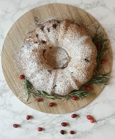 a cranberry bunt cake on a wooden platter with berries and rosemary