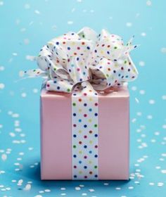 a pink gift box with white and multicolored polka dots on it sitting on a blue surface