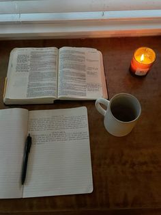 an open book with a cup of coffee next to it and a candle on a table