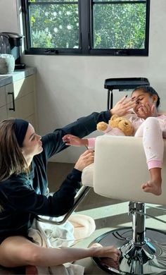 a woman sitting in a chair with a baby on her lap and another person holding a teddy bear