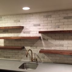 a kitchen with white brick walls and wooden shelvings on the wall, as well as a stainless steel sink