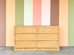 an empty wicker dresser in front of a multicolored wall with vertical stripes