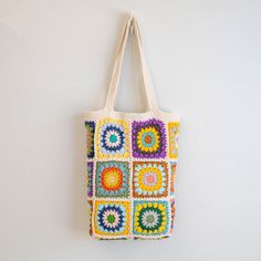 a multicolored crocheted tote bag hanging on a wall with white background