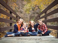 three children sitting on a bridge in the fall