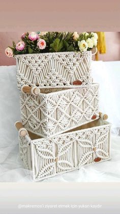 two crocheted baskets with flowers in them sitting on a white bedding sheet