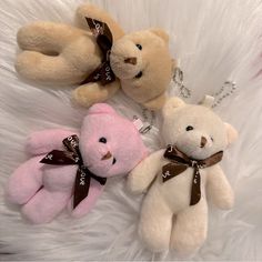 three stuffed teddy bears are laying on a white fur covered surface, one has a brown ribbon around its neck and the other is pink